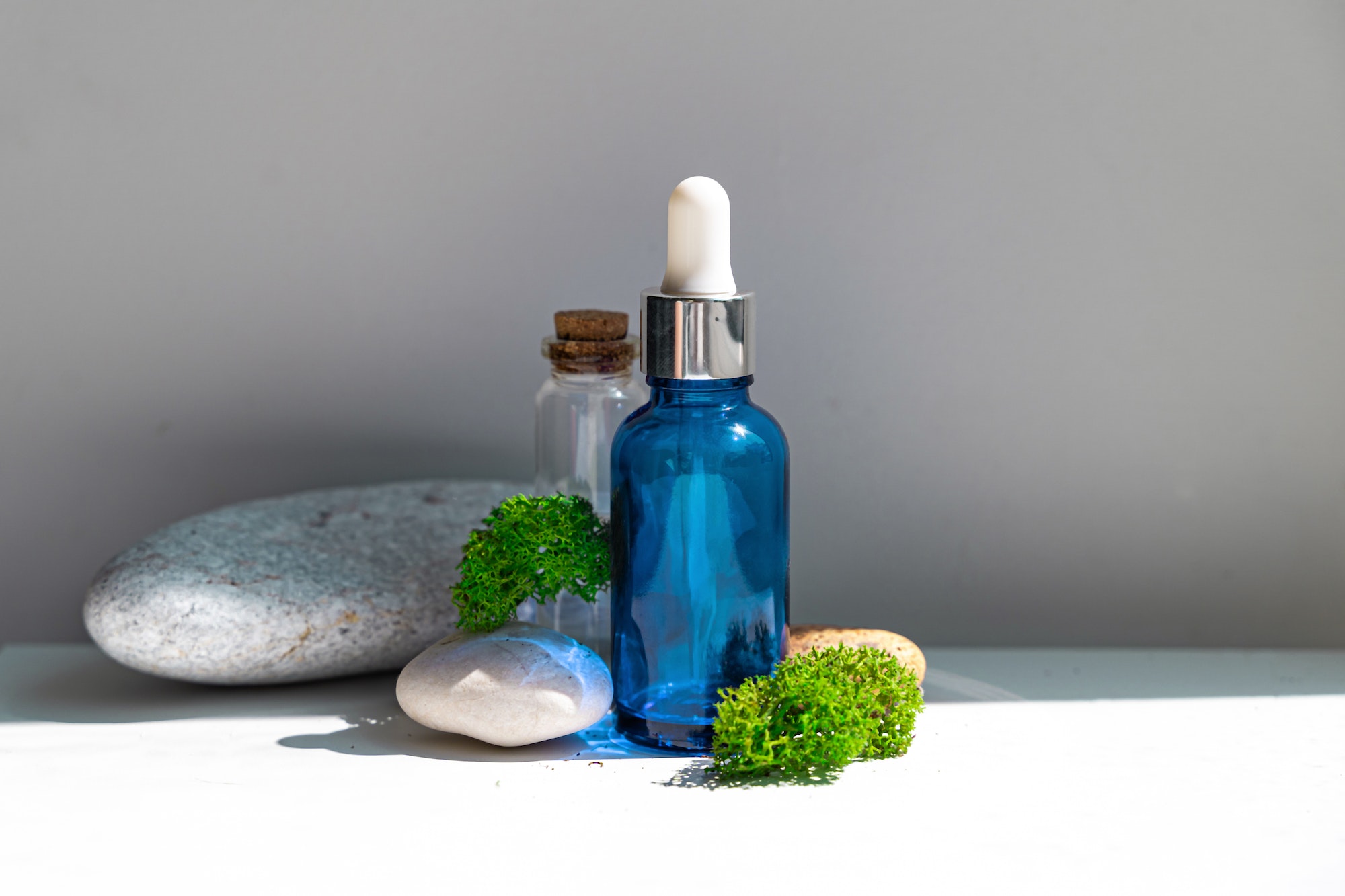 Sea moss personal care. Blue bottle with oil dropper and sea stones and moss on white background